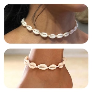 Könnte beinhalten: Eine weiße Muschel-Choker-Halskette und ein passendes Fußkettchen. Der Schmuck besteht aus mehreren kleinen, cremefarbenen Muscheln, die auf einer weißen Schnur aufgereiht sind. Die Halskette liegt um einen Hals und das Fußkettchen um einen Knöchel.