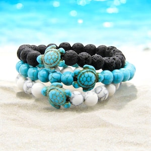 May include: Three stacked bracelets with turquoise and white beads and black lava rock beads. Each bracelet features a small turquoise turtle charm.