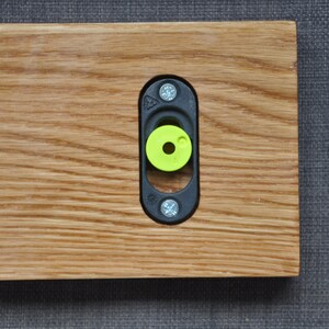 May include: A close-up of a wooden shelf with a black metal bracket and a green plastic spacer. The bracket is attached to the shelf with screws.