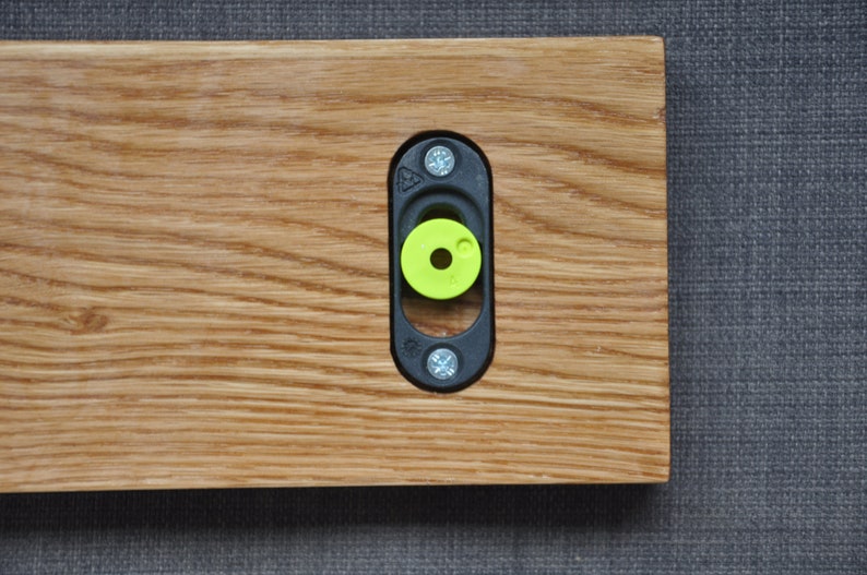 May include: A close-up of a wooden shelf with a black metal bracket and a green plastic spacer. The bracket is attached to the shelf with screws.