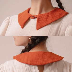 May include: A burnt orange, textured collar with a rounded shape and a small tie closure. The collar is worn over a white, textured blouse. The image shows the collar from the front and back. The text "Stitch Maiden" is visible in the upper right corner.