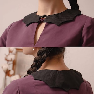 May include: A purple blouse featuring a distinctive black collar with a unique shape and a small clasp fastening. The blouse is made of a soft material. The image is well-lit, highlighting the collar and blouse details. The Stitch Maiden logo is visible in the top right corner.