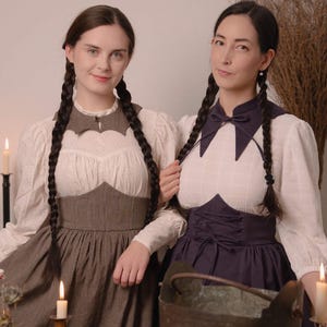 May include: Two women in vintage dresses with long plaits. The dresses have white blouses, dark bodices, and long skirts. One dress is brown, the other is dark blue. The image has a vintage aesthetic with candles and a cauldron.