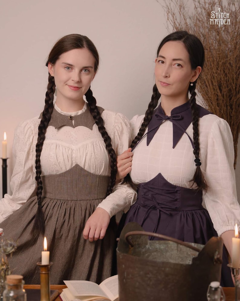 May include: Two women in vintage dresses with long plaits. The dresses have white blouses, dark bodices, and long skirts. One dress is brown, the other is dark blue. The image has a vintage aesthetic with candles and a cauldron.