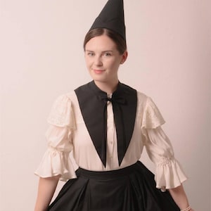 May include: A person wearing a black, pointed hat and a black and white outfit. The outfit includes a black collar with a bow, a white blouse with lace sleeves, and a black skirt. The image has the text "Stitch Maiden" in the upper right corner.