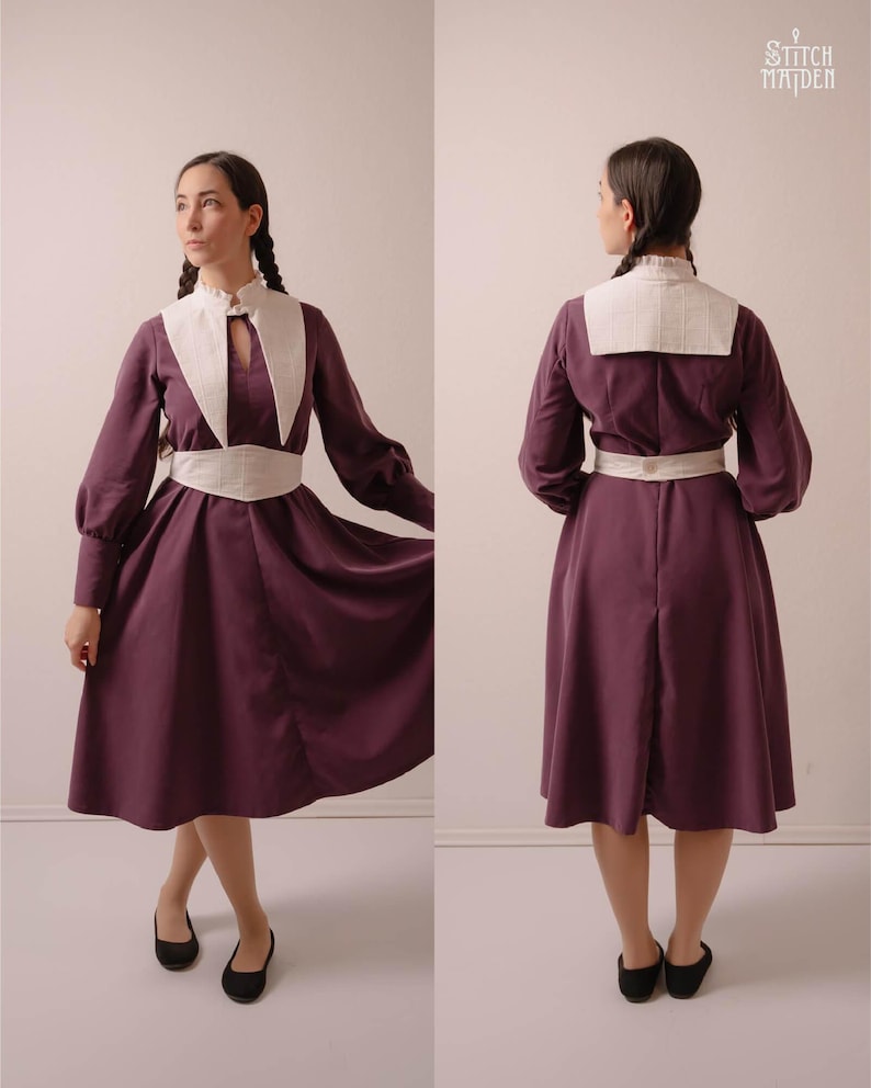 May include: A plum-coloured dress with long sleeves, a white collar, and a matching white belt. The dress has a keyhole neckline and a flared skirt. The sleeves are gathered at the cuffs. The model is wearing black flats. The dress is from Stitch Maiden.