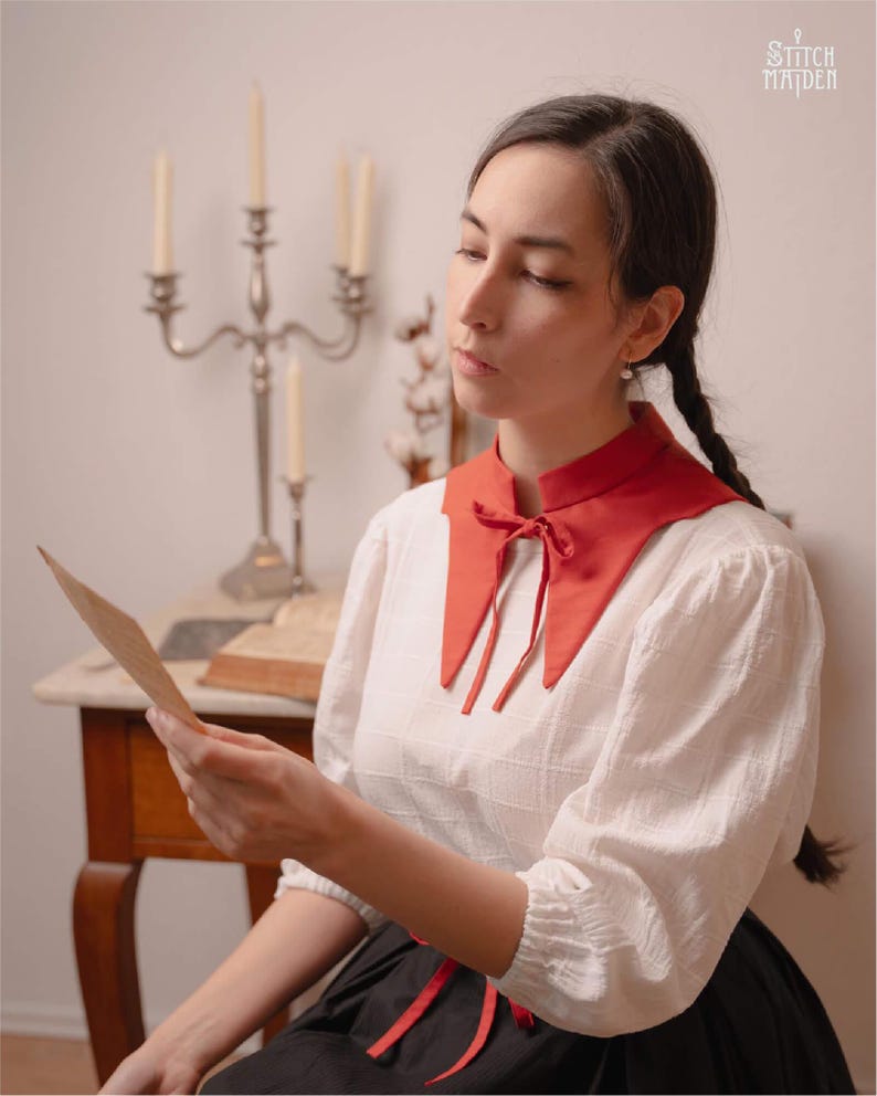 May include: A white blouse with a red collar and a black skirt. The red collar is tied with a bow. The blouse has long sleeves. The image also shows a silver candelabra and the text "STITCH MAIDEN".
