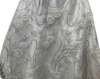 Puede incluir: Tela blanca con bordado floral plateado. La tela tiene una textura delicada y transparente y presenta intrincados patrones florales con lentejuelas y cuentas plateadas.