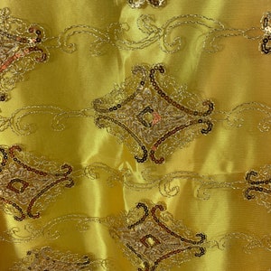 May include: Yellow fabric with a gold and brown embroidered design. The design features intricate swirls and diamond shapes.