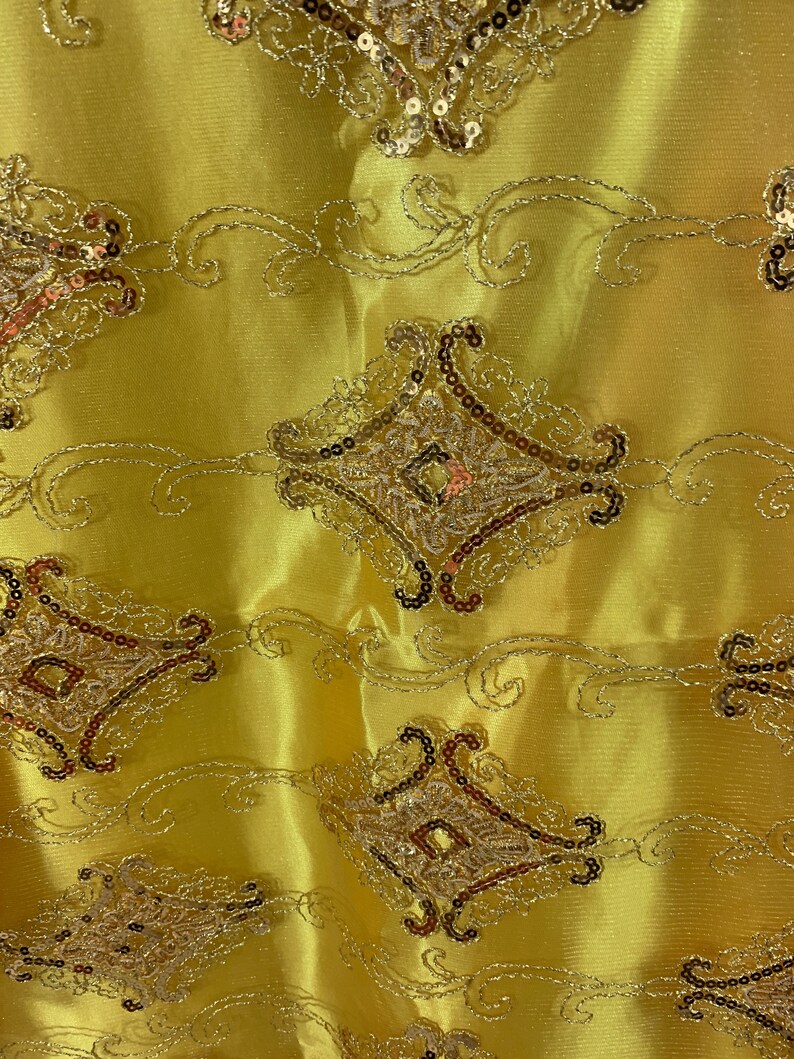 May include: Yellow fabric with a gold and brown embroidered design. The design features intricate swirls and diamond shapes.
