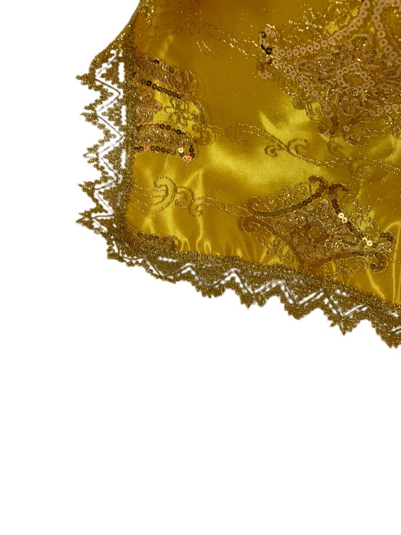 May include: Gold fabric with a decorative pattern and gold sequins. The fabric has a gold lace trim.