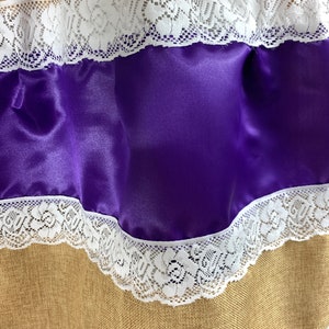 May include: A brown burlap fabric with two layers of white lace trim and a layer of purple satin fabric.