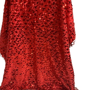 May include: Red fabric with a sequined pattern. The fabric has a silver trim around the bottom edge.