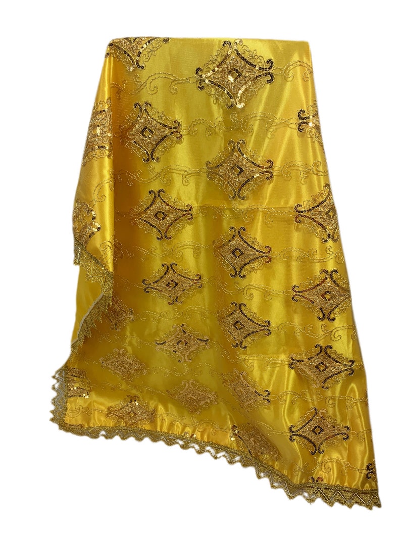 May include: A gold fabric tablecloth with a decorative pattern of gold and black sequins. The tablecloth has a scalloped edge.