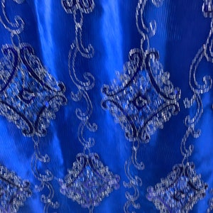 Puede incluir: Tela azul con un dise&ntilde;o estampado en plata y azul. La tela tiene un brillo sutil y una superficie texturizada.