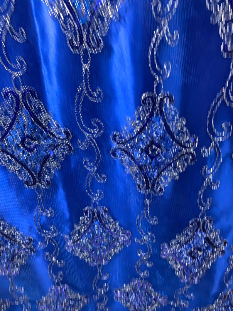 Puede incluir: Tela azul con un dise&ntilde;o estampado en plata y azul. La tela tiene un brillo sutil y una superficie texturizada.