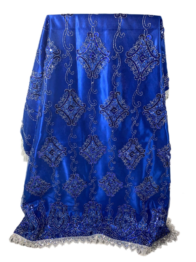 Puede incluir: Tela azul real con un patr&oacute;n bordado en plata y azul. La tela tiene un acabado satinado brillante y un ribete de flecos plateado y azul.