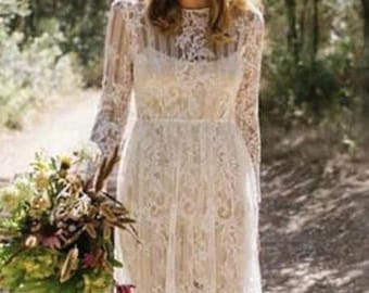 May include: A white lace wedding dress with long sleeves and a flowing skirt. The dress has a fitted bodice and a delicate floral pattern. The bride is wearing a flower crown and holding a bouquet of flowers.