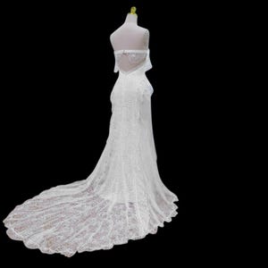 May include: A white, strapless wedding gown with a long train. The dress is made of lace and features a fitted bodice and a flowing skirt. The back of the dress has a keyhole design and is displayed on a mannequin.