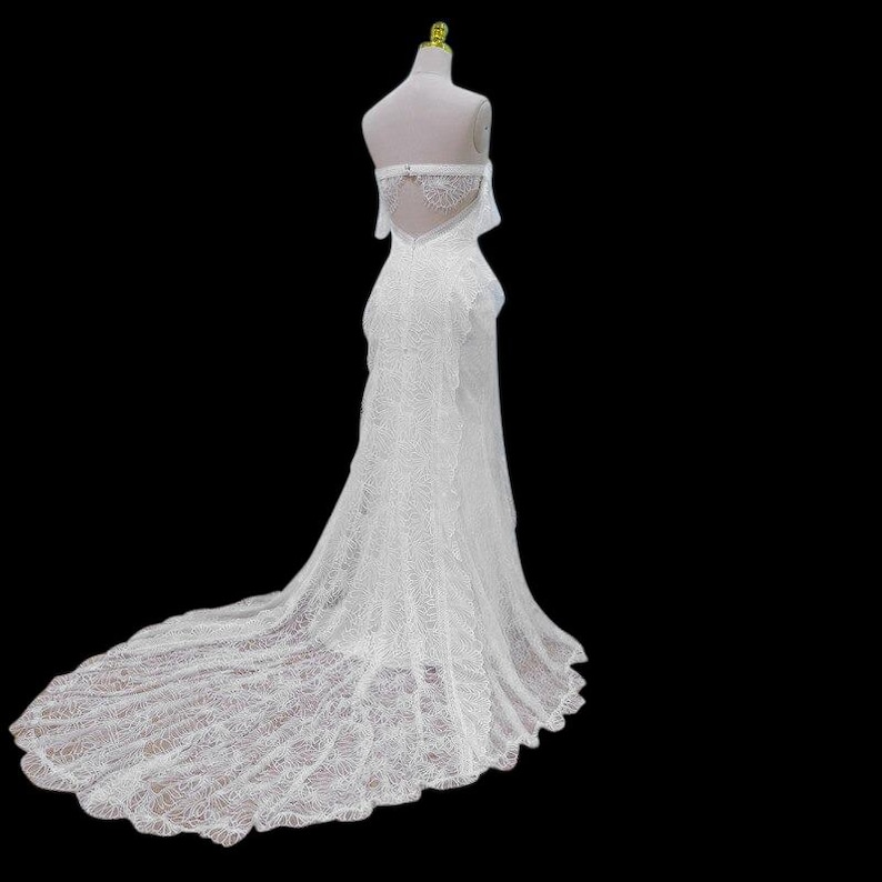 May include: A white, strapless wedding gown with a long train. The dress is made of lace and features a fitted bodice and a flowing skirt. The back of the dress has a keyhole design and is displayed on a mannequin.