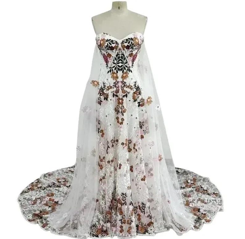 Pu&ograve; includere: Un abito da sposa bianco senza spalline con un motivo floreale e un lungo strascico. L'abito ha una scollatura a cuore ed &egrave; realizzato in pizzo.