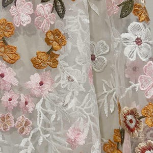 Pu&ograve; includere: Tessuto bianco trasparente con ricami floreali in rosa, arancio e verde.