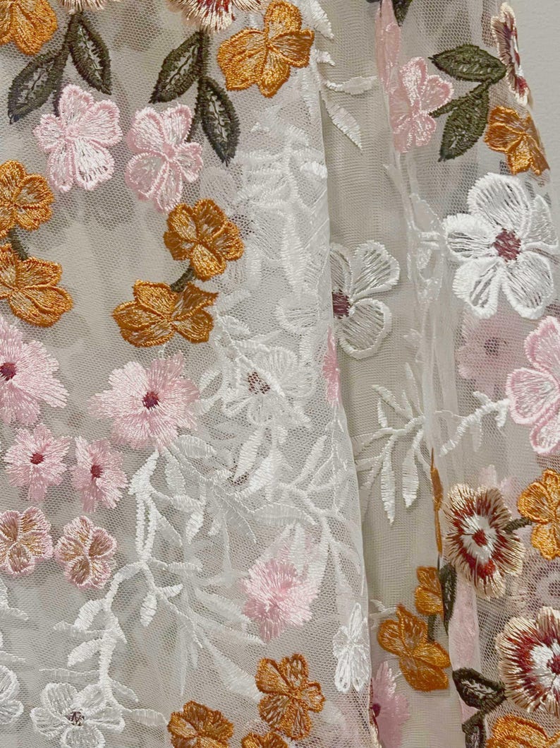 Pu&ograve; includere: Tessuto bianco trasparente con ricami floreali in rosa, arancio e verde.