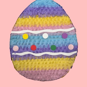May include: An Easter egg-shaped piñata with a colorful design. The piñata features layers of yellow, purple, blue, and pink fringed paper. White wavy lines and colorful circles decorate the front. A festive decoration for Easter celebrations.