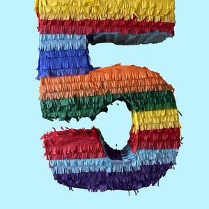 May include: A rainbow-colored pinata shaped like the number 5. The pinata is made of tissue paper and has a yellow, red, blue, green, and purple color scheme.