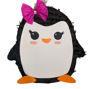 May include: A penguin piñata with a black body and white face. The penguin has large black eyes, orange feet, and a bright pink bow. The piñata is decorated with black fringe and is ready to be filled with treats.