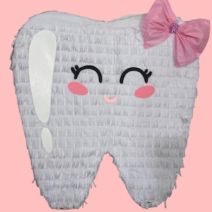 May include: A white tooth-shaped piñata with a smiling face, pink cheeks, and a pink bow. The piñata has a textured surface and a large exclamation point on the side. The background is a solid pink color.