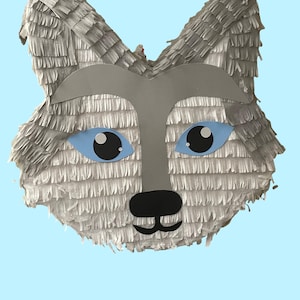 May include: A gray wolf piñata with blue eyes and a black nose. The piñata is made of tissue paper and is shaped like a wolf's head.