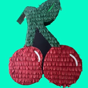 May include: A red and green cherry-shaped pinata. The pinata is made of tissue paper and has a green stem and leaves.