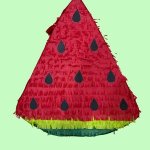 May include: A triangular watermelon piñata covered in red, yellow, and green fringe paper. The red section features several black teardrop-shaped paper cutouts representing seeds. The bottom edge has a layer of yellow fringe above a green base.