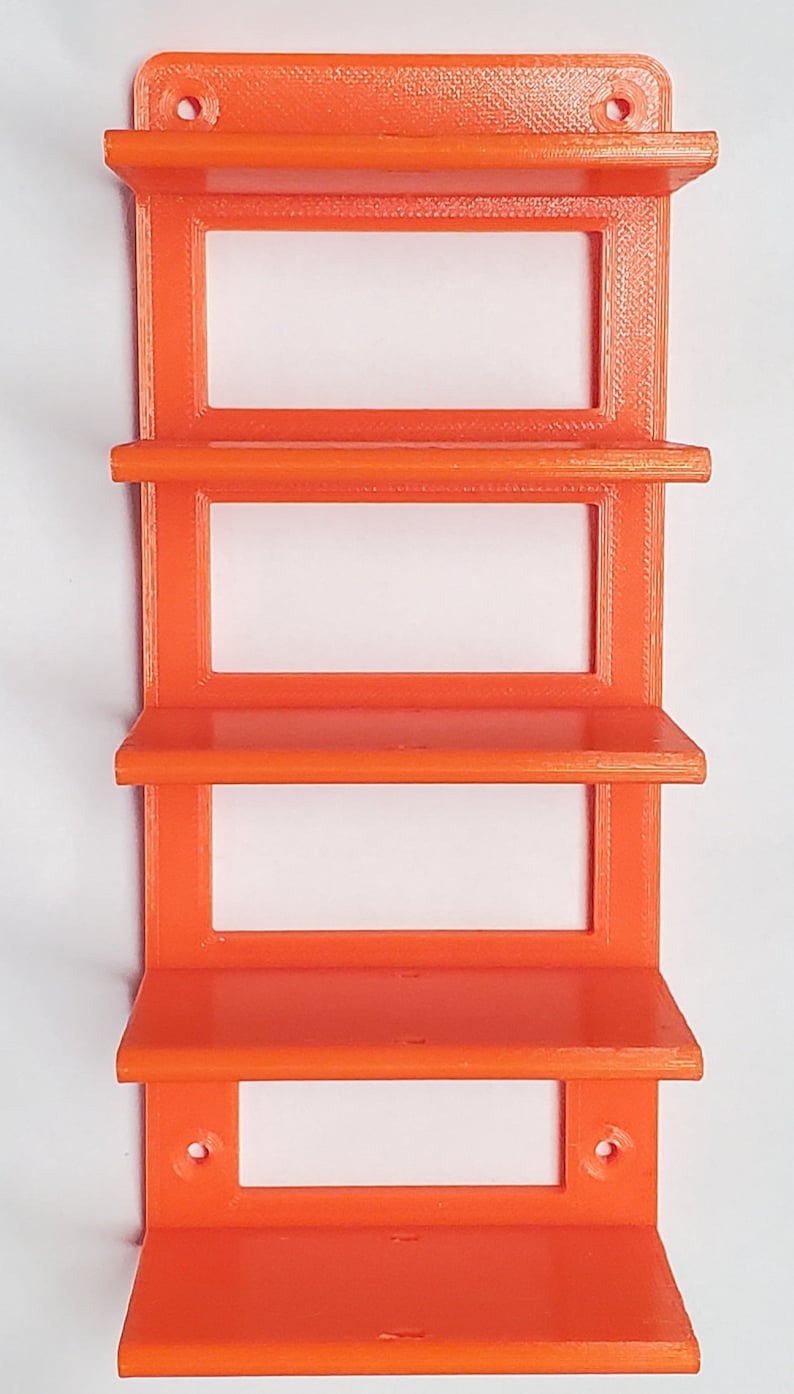 K&ouml;nnte beinhalten: Orangenes, 3D-gedrucktes Wandregal mit vier rechteckigen Ablagen. Das Regal hat eine rechteckige R&uuml;ckseite mit zwei L&ouml;chern zur Befestigung. Die Ablagen sind gleichm&auml;&szlig;ig angeordnet und haben eine Lippe an der Vorderkante. Das Regal ist aus Kunststoff.