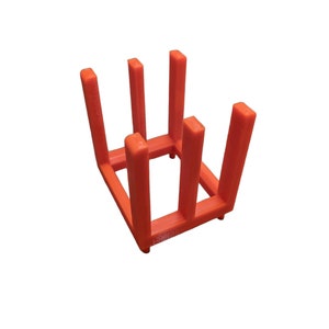 May include: An orange, 3D-printed, square-shaped rack with six vertical supports. The rack is designed to hold items and is made of a solid, vibrant orange plastic. The supports are evenly spaced and the base has small feet.