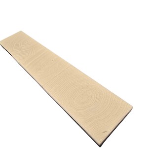 Pu&ograve; includere: Una tavola di legno rettangolare di colore beige chiaro con un motivo a venature visibile. La tavola ha un bordo scuro ed &egrave; angolata su uno sfondo bianco. Le venature del legno mostrano motivi circolari.