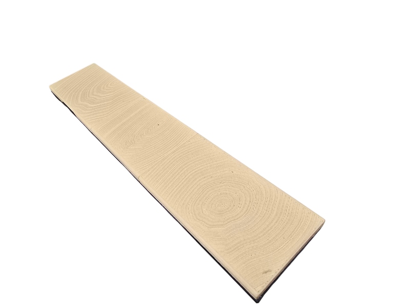 Pu&ograve; includere: Una tavola di legno rettangolare di colore beige chiaro con un motivo a venature visibile. La tavola ha un bordo scuro ed &egrave; angolata su uno sfondo bianco. Le venature del legno mostrano motivi circolari.