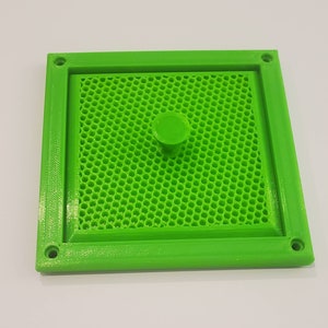 May include: A bright green square frame with a honeycomb pattern inside. The frame has a small, round, green knob in the center.