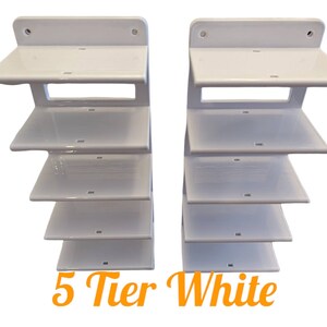 K&ouml;nnte beinhalten: Zwei wei&szlig;e 5-st&ouml;ckige Wandregale. Jedes Regal hat eine flache Oberseite und ein abgestuftes Design. Die Regale bestehen aus gl&auml;nzendem wei&szlig;em Material. Der Text "5 Tier White" steht in orangefarbener Schrift unten.