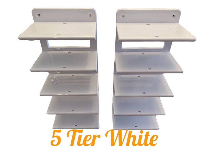 K&ouml;nnte beinhalten: Zwei wei&szlig;e 5-st&ouml;ckige Wandregale. Jedes Regal hat eine flache Oberseite und ein abgestuftes Design. Die Regale bestehen aus gl&auml;nzendem wei&szlig;em Material. Der Text "5 Tier White" steht in orangefarbener Schrift unten.
