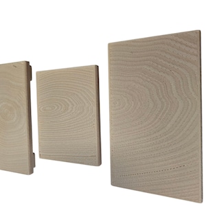 Pu&ograve; includere: Tre blocchi di legno rettangolari di diverse dimensioni, disposti uno accanto all'altro. I blocchi sono di colore chiaro, forse non rifiniti, e mostrano motivi di venature del legno visibili. La venatura del legno crea una texture naturale e organica.