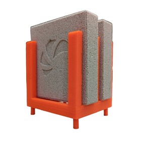 May include: An orange 3D-printed holder with three gray rectangular cleaning pads. The holder has a square base with four small legs and vertical supports to hold the pads in place. The center pad has a decorative design.