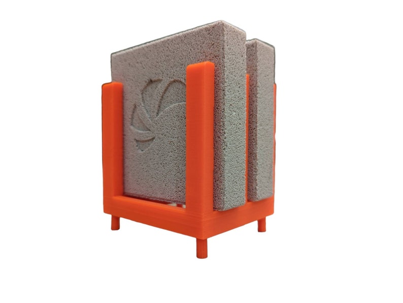 May include: An orange 3D-printed holder with three gray rectangular cleaning pads. The holder has a square base with four small legs and vertical supports to hold the pads in place. The center pad has a decorative design.