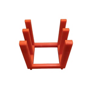 May include: An orange, 3D-printed, rectangular stand with a series of vertical supports. The stand is designed to hold items upright. The stand is made of a solid, opaque material and is set against a white background.