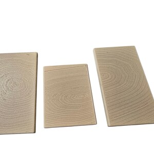 Pu&ograve; includere: Tre blocchi di legno non rifiniti con motivi di venature visibili. I blocchi sono rettangolari, uno dei quali ha una forma trapezoidale. Il legno ha un colore chiaro e naturale, e la venatura crea motivi circolari.
