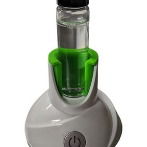 May include: A white and green essential oil diffuser with a clear glass bottle containing liquid. The diffuser has a power button and a green plastic ring around the bottle.