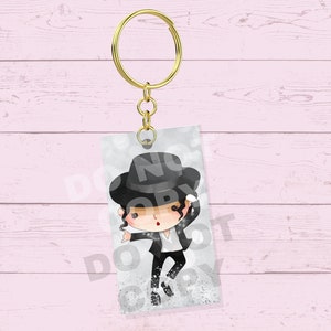 May include: A keychain featuring a cartoon illustration of a performer in a black suit, hat, and white shirt. The keychain has a gold-colored ring and chain. The background is a light gray with a subtle pattern.