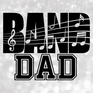May include: Black graphic design with the words "BAND DAD" in bold, outlined letters. Musical notes and a treble clef are integrated into the word "BAND". The background is a light, sparkly gray.