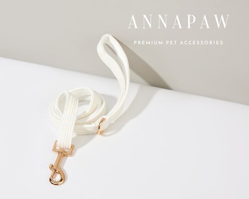 K&ouml;nnte beinhalten: Hunde-Leine aus wei&szlig;em Baumwollstoff mit einem goldenen Metallverschluss. Die Leine ist aufgerollt und der Markenname "ANNAPAW PREMIUM PET ACCESSORIES" ist oben im Bild zu sehen.